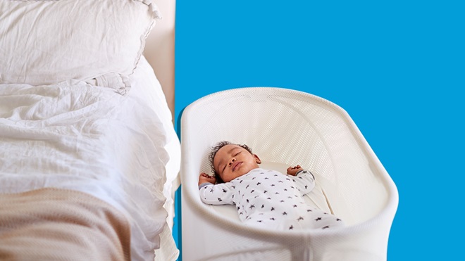 baby sleeping in a bassinet beside a bed